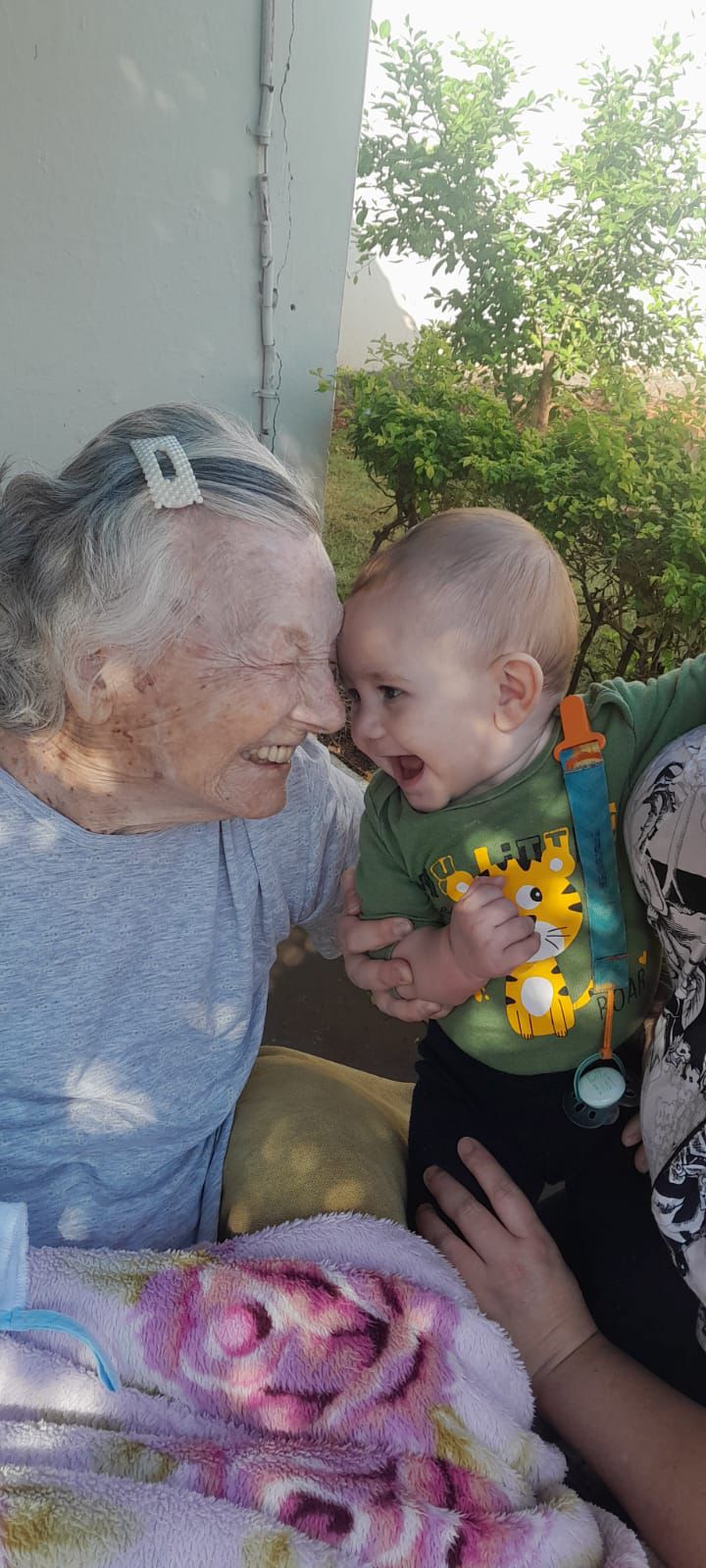 Senhora idosa sorrindo com bebê no colo que está vestindo roupa verde